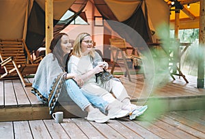 Two young women friends drinking tea and relaxing in glamping in the woods