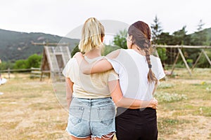 Two young women friends on her back with hair in a braid and blonde hair hugging each other in the countryside. Friendship concept