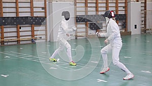 Two young women in full protection having an active fencing training in the school gym