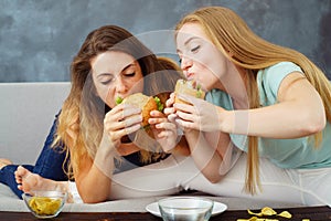 Two young women greedily eating burgers and chips