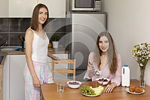 Two young women have breakfast together at home in the kitchen