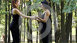 Two young women have a workout in black suits in a park in slo-mo