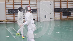 Two young women having an active fencing training in the school gym