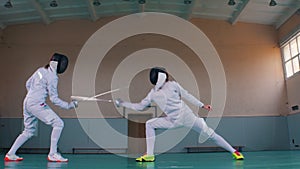 Two young women having an active fencing training in the school gym