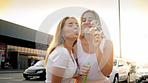 Two young women having fun and blowing soap bubble on city street