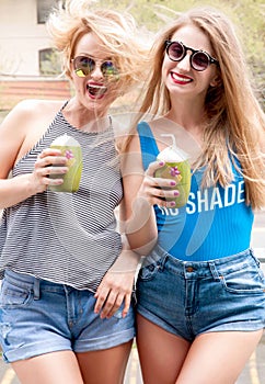 Two young women having fun and drinking cocktail in summer day