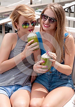 Two young women having fun and drinking cocktail in summer day