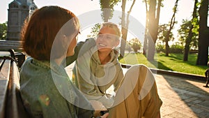 Two young women having fun, talking while sitting on the bench in the city park. Lesbian couple spending time together