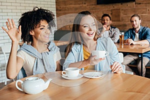 Two young women having tea in cafe and men sitting at next table looking photo