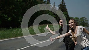Two young women hitchhikers stand on the sidelines and ask to stop the passing cars