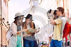 Two young women hold city map and guy with camera