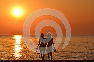 Two young women holding hands walking barefoot with slippers in his hand on the beach