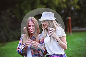 Two young women holding hands walking in green park. Best friends