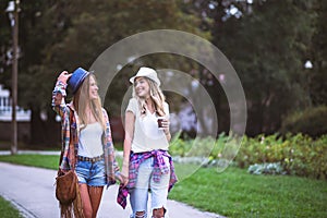 Two young women holding hands walking in green park. Best friends