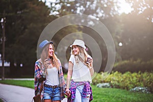 Two young women holding hands walking in green park. Best friends