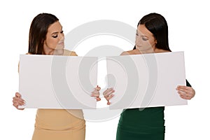 Two young smiling women holding two pieces of blank paper, looking down on papers