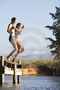 Two Young Women Jumping From Jetty Into Lake