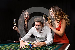 Two young women and man behind roulette table on black background