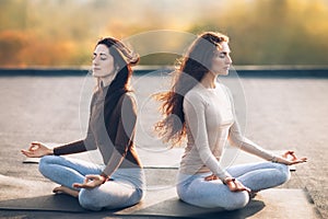 Two young women meditating in Lotus Pose on the roof outdoor