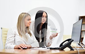 Two young women office workers are discussion and looking at the monitor