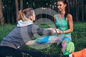 Two young women performing partner yoga pose, double seated straddle, stretching their leg and back muscles sitting on