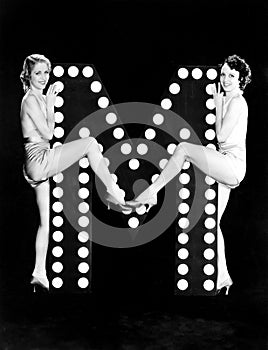 Two young women posing with the letter M