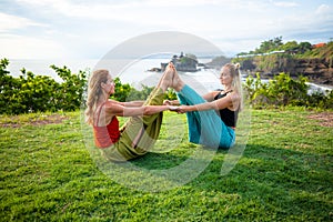 Two young women practice Ubhaya Padangusthasana, Wide-Angle Seated Forward Bend. Strengthen legs and core. Tanah Lot temple, Bali photo