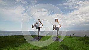 Two young women practice yoga on beach by the sea or ocea. Training Standing Hand to Toe pose and then Standing Half