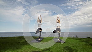 Two young women practice yoga on beach by the sea or ocea. Training Standing Hand to Toe pose and then Standing Half