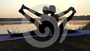 Two Young Women Practice Yoga Sitting on Mats Back-To-Back at Sunset in Slo-Mo