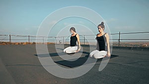 Two young women practicing hatha yoga on the roof, outdoors