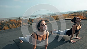 Two young women practicing yoga asana on the roof, outdoors in morning