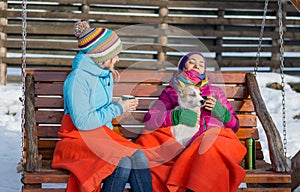 Two young women relaxing in a wooden rocking chair on a chilly w