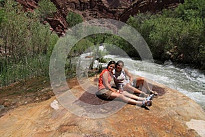 Two young women rest by Tapeats Creek on backpacking trip in Grand Canyon.