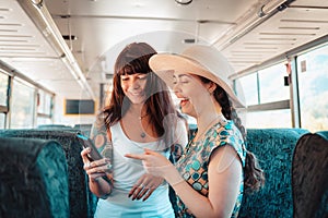 Two young women ride on public transport and cheerfully watch something on their smartphone. Concept of communication and social