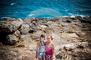 Two young and women on the rocks near the wild ocean. Storm, huge waves coming and splashing. Tropical island Nusa