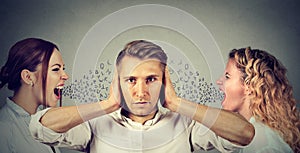 Two young women screaming at a calm man covering his ears with hands ignoring them.