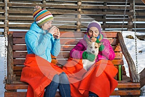 Two young women sipping hot coffee in a wooden rocking chair on