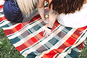 Two young women sit side by side on a bright plaid blanket in nature