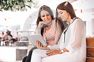 Two young women sitting on a bench and watching videos in a tablet