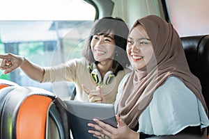 two young women smiling with pointing fingers while chatting while holding a tablet