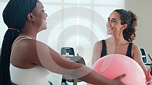 Two young woman in sportswear workout routines using exercise ball in fitness gym with trainer.