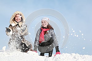 Two young women squatting and throw snow