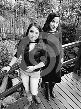 two young women stand posing on the bridge of a botanical garden