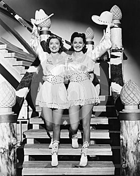 Two young women stepping down a staircase waving their western hats