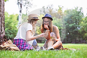 Two young women students in park sitting on grass talking
