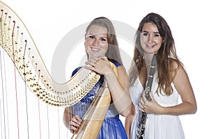 Two young women in studio with harp and clarinet against white b