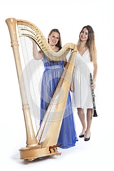 Two young women in studio with harp and clarinet against white b