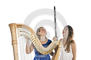 Two young women in studio with harp and clarinet against white b