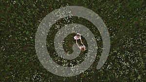 Two young women in summer dresses holding hands and dancing in the field of daises